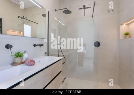 Modernes Bad mit großer bodenebener Glasdusche, schwarzen Armaturen und einem geräumigen Doppelwaschtisch mit Naturholzoberfläche. Stockfoto