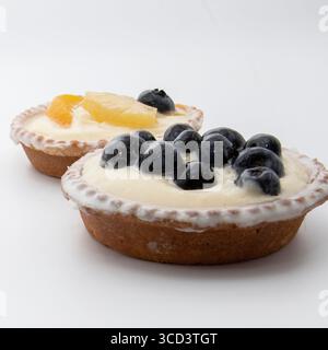 Nahaufnahme von zwei Obstkuchen mit cremiger Pustard-Füllung. Eine mit Heidelbeeren, die andere mit Kiwi, Pfirsich, Ananas und einer Heidelbeere. Deliciou Stockfoto