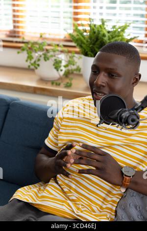 Afroamerikaner in gelbem T-Shirt, der im Heimstudio mit Popfilter ins Mikrofon spricht Stockfoto