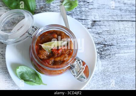 Zacusca: Traditionelle rumänische Aufstrich. Ein Glas mit einer cremigen Gemüsesauce, Auberginen, Zwiebeln, Tomaten und gebratenen Paprika auf hölzernem Hintergrund. Stockfoto