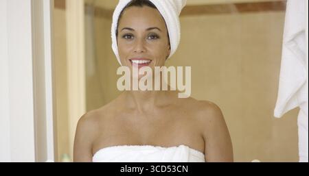 Schöne junge Erwachsene Frau, die sich am Eingang der Duschkabine oder der Sauna beugte, während sie in Handtücher gewickelt war Stockfoto