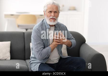 Ein älterer Mann, der zu Hause an Brustschmerzen leidet Stockfoto