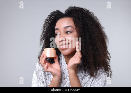 Schöne brasilianische Frau mit einem Glas Kollagencreme auf grauem Hintergrund Stockfoto