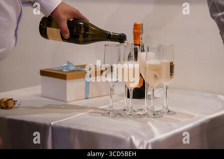 Ein Kellner gießt während einer feierlichen Veranstaltung Champagner in Flötengläser. Eine Geschenkbox auf einer weißen Tischdecke sorgt für eine luxuriöse Atmosphäre Stockfoto