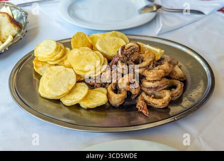 Eine Platte mit traditionellen gebratenen Calamari (Tintenfischringe) und Kartoffeln, ein beliebtes mediterranes Meeresfrüchte-Gericht, das in einem Restaurant serviert wird Stockfoto