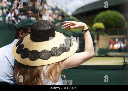Eine junge Frau mit einem großen Strohhut auf einem der Außenplätze bei den Wimbledon Championships 2025 in London, England, Großbritannien Stockfoto