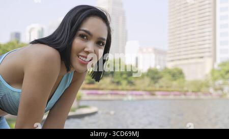 Eine fröhliche, fitte Frau macht eine Pause während ihres Outdoor-Workouts in einem sonnigen Stadtpark und verkörpert einen gesunden Lebensstil Stockfoto