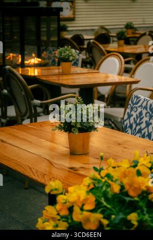 Gemütliches Café im Freien mit Holztischen, Topfpflanzen und warmer Beleuchtung Stockfoto