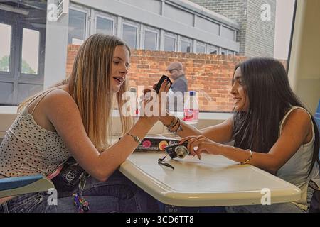 Norwood, South London, Großbritannien 29. Juli 2025 zwei junge Frauen in einem Pendlerzug tauschen photoÕs auf ihren Digitalkameras aus. Hinweis: Keine Smartphones Stockfoto