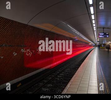 Stockholm, Schweden - 10. Juni 2025: Eine U-Bahn fährt durch eine U-Bahn-Station und hinterlässt eine Rotlichtspur. Stockfoto