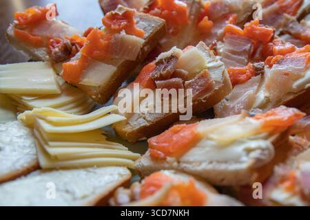 Blick von oben auf verschiedene offene Sandwiches mit gesalzenem Fisch, Speck und Butter auf Brotscheiben, begleitet von Käse. Rustikale hausgemachte Vorspeise, P Stockfoto