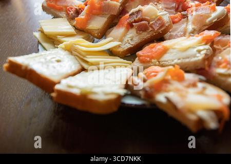 Blick von oben auf verschiedene offene Sandwiches mit gesalzenem Fisch, Speck und Butter auf Brotscheiben, begleitet von Käse. Rustikale hausgemachte Vorspeise, P Stockfoto