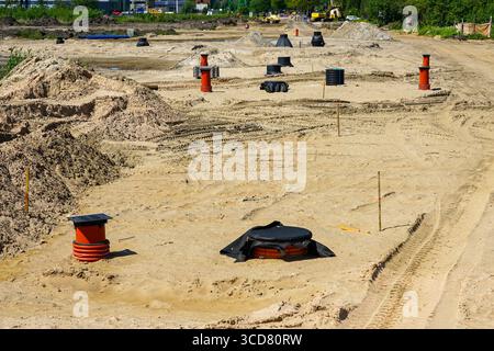 Freiliegende Schächte und Versorgungsleitungen auf einer Sandbaustelle während der frühen Phase der Infrastrukturinstallation an einem klaren Tag Stockfoto