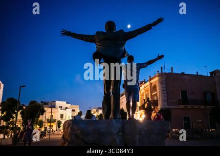 Silhouette für einen Mann, der für ein Foto posiert, das die Statue von Domenico Modugno in Polignano nachahmt. Eine Stute bei Nacht mit dem Mond im Hintergrund, Apulien. Stockfoto