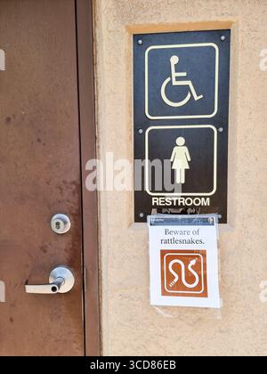 Vorsicht vor Klapperschlangen; es wurde ein Schild mit einer Warnung für Schlangen an der Toilette für Frauen und Behinderte hinzugefügt Stockfoto
