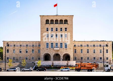 Ein großes, symmetrisches Regierungsgebäude mit einem zentralen Turm und einer roten Flagge auf der Oberseite, mit Bogenfenstern und einer Steinfassade. Fahrzeuge sind geparkt Stockfoto