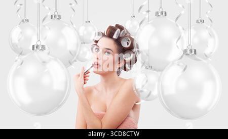Weihnachtsschmuck. Glückliche Frau, die Lippenstift aufträgt, umgeben von transparenten Weihnachtsschmuck. Werbebanner für Feiertage mit Kopie Stockfoto