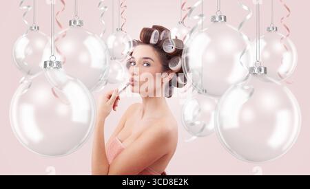 Weihnachtsschmuck. Glückliche Frau, die Lippenstift aufträgt, umgeben von transparenten Weihnachtsschmuck. Werbebanner für Feiertage mit Kopie Stockfoto