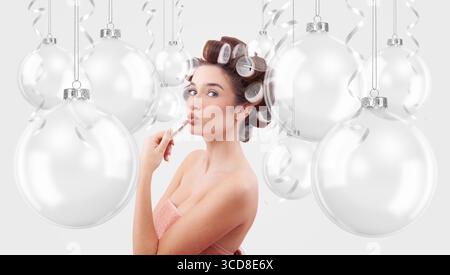 Weihnachtsschmuck. Glückliche Frau, die Lippenstift aufträgt, umgeben von transparenten Weihnachtsschmuck. Werbebanner für Feiertage mit Kopie Stockfoto