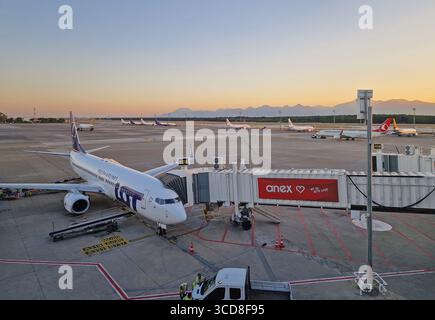 ANTALYA, TÜRKEI - 5. JULI 2025 Antalya Flughafenszene bei Sonnenuntergang und ein Flugzeug an der Jetbrücke mit anderen Flugzeugen sichtbar auf dem Asphalt. Distan Stockfoto