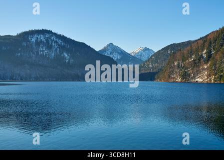 Dieses hochauflösende Foto zeigt eine ruhige, bergige Szene am See unter klarem blauen Himmel. Im Mittelpunkt steht ein ruhiger, reflektierender See Stockfoto
