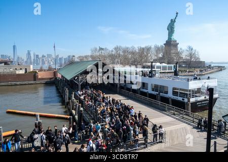 Blick vom Boot aus, bevor Sie nach Liberty Island fahren, mit Aussichtspersonen, die auf das Boot warten, mit Manhattan in der Ferne Stockfoto