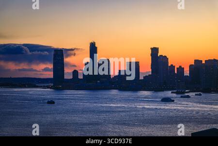 Die Silhouette der Skyline von Jersey City aus New York City mit einem dramatischen Sonnenuntergang und farbenfrohen Wolken über dem Hudson River in New Jersey, USA Stockfoto