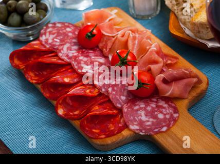 Spanische leckere Gerichte, die Würstchen und Schinken mit Tomaten am Holzschreibtisch schneiden Stockfoto