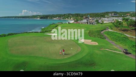 Zwei Golfspieler spielen auf einem üppig grünen Golfplatz mit Blick auf das Meer in Bali, Indonesien, und genießen die atemberaubende Aussicht und das tropische Wetter Stockfoto