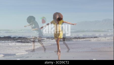 Eine sich drehende Frau in gelbem Kleid, die entlang des nassen Sandes am Meeresrand läuft, mit schwimmendem Strandball Stockfoto