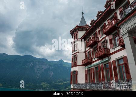 Grandes historisches Alpenhotel mit roten Balkonschaltern und einem Turmspitz gegen bewölkte Berggipfel in Europa. Stockfoto