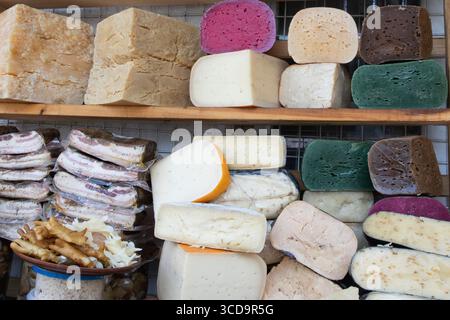 Eine Auswahl an geräucherten Speckblöcken, bunten Käsesorten, Würstchen und Snacks, die auf dem Marktstand ausgestellt werden, sowie eine Auswahl an traditionellen lokalen Speisen. Stockfoto