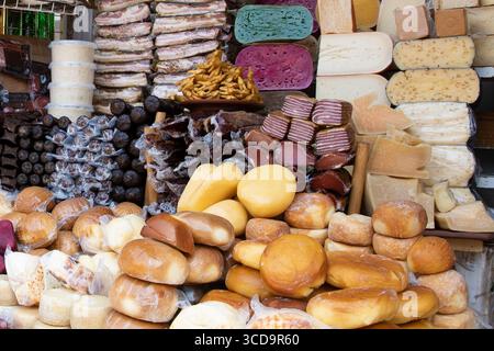 Vielfalt an bunten Käsesorten und geräucherten Fleischsorten auf einem Holzstand auf einem traditionellen Markt. Rustikale Speisen mit natürlichen Texturen und handwerklichen Produkten Stockfoto