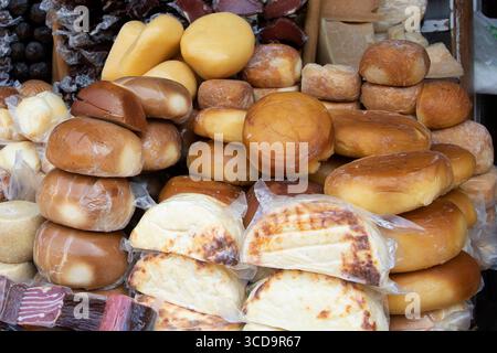 Vielfalt an bunten Käsesorten und geräucherten Fleischsorten auf einem Holzstand auf einem traditionellen Markt. Rustikale Speisen mit natürlichen Texturen und handwerklichen Produkten Stockfoto