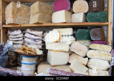 Eine Auswahl an geräucherten Speckblöcken, bunten Käsesorten, Würstchen und Snacks, die auf dem Marktstand ausgestellt werden, sowie eine Auswahl an traditionellen lokalen Speisen. Stockfoto