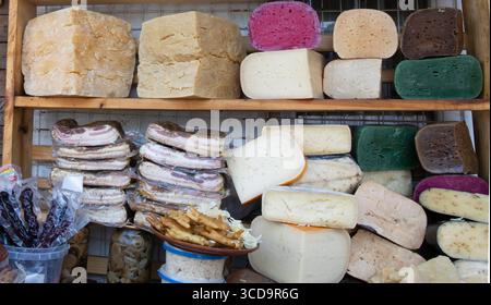 Eine Auswahl an geräucherten Speckblöcken, bunten Käsesorten, Würstchen und Snacks, die auf dem Marktstand ausgestellt werden, sowie eine Auswahl an traditionellen lokalen Speisen. Stockfoto