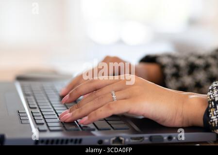 Nahaufnahme einer Frauenhände, die auf einer Laptop-Tastatur tippen. Ihre Finger sind mit einem Ring verziert. Der Fokus liegt scharf auf ihren Händen und der Tastatur, während t Stockfoto