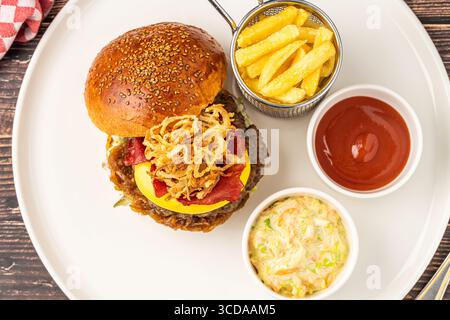 Köstlicher Gourmet-Burger mit Cheddar-Käse, gebratenen Zwiebeln, Krautsalat und Pommes frites Stockfoto