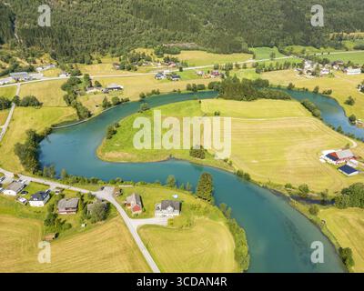 Aus der Vogelperspektive auf den sich windenden Stryn River, der den klaren Himmel wie ein türkisfarbenes Band zwischen grünen Feldern und verstreuten Häusern reflektiert, Stryn, Vestland, Norwegen. Stockfoto