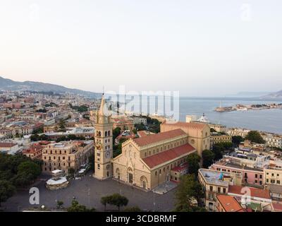 Aus der Vogelperspektive auf die goldene Fassade des Duomo und den Glockenturm werfen lange Schatten über die Piazza del Duomo, mit der Meerenge von Messina in der Ferne, Messina, Sizilien, Italien. Stockfoto