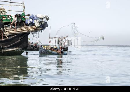 Cox's Bazar, Bangladesch - 29. November 2022: Blick auf Fischer, die Netze von ihren Booten auf dem ruhigen, glitzernden Wasser der Bucht unter einem hellen, weiten Himmel werfen. Stockfoto