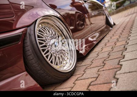 Rom, italien 18. juli 2025, burgunderroter Lowrider bmw e36 parkte auf Ziegelsteinpflastern mit Chrom- und Gold-bbs rs-Rädern Stockfoto