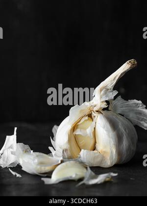 Ganze Knoblauchzwiebeln mit losen Zehen und papieriger Haut auf dunklem Hintergrund. Stockfoto