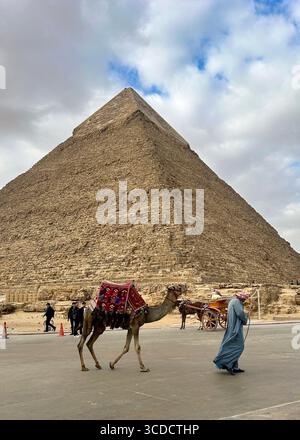 Ein Beduinenmann bietet Touristen einen Kamelritt in der Nähe der Großen Pyramide von Gizeh, einer berühmten archäologischen Stätte in Ägypten. Stockfoto