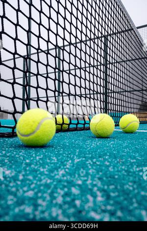 Ein niedriger Blickwinkel auf Padel-Kugeln, die auf einem türkisfarbenen Platz in der Nähe des Netzspielerperspektivkonzepts verstreut sind Stockfoto