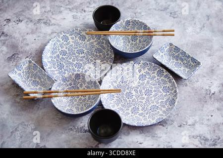 Leere Keramikschalen, Teller und Essstäbchen im orientalischen Stil auf grauem Steinhintergrund mit Kopierraum. Draufsicht Stockfoto