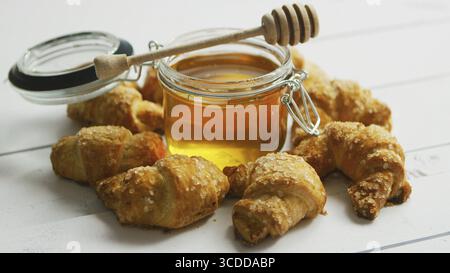 Glas Glas voller Honig mit hölzernen Spindel durch frische Croissants auf weißem Hintergrund Holz umgeben Stockfoto