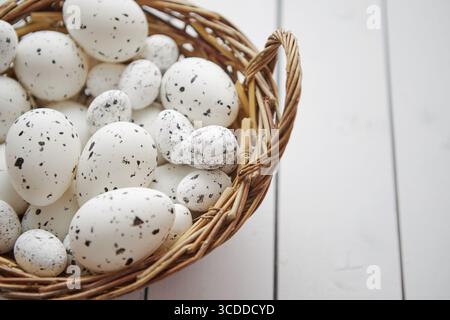 Korb mit Hühnchen und Wachteln weiß gepunktete Ostereier in braunem Korb. Auf weißem Holztisch Stockfoto