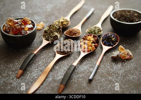 Löffel mit verschiedenen Arten trockener Teeblätter auf rostigem dunklem Hintergrund. Draufsicht Stockfoto