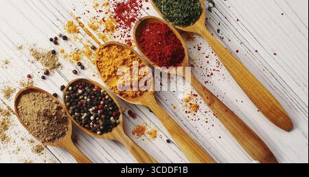 Blick von oben auf angeordnete Holzlöffel gefüllt mit einer bunten Auswahl an Gewürzen auf weißem Holztisch Stockfoto